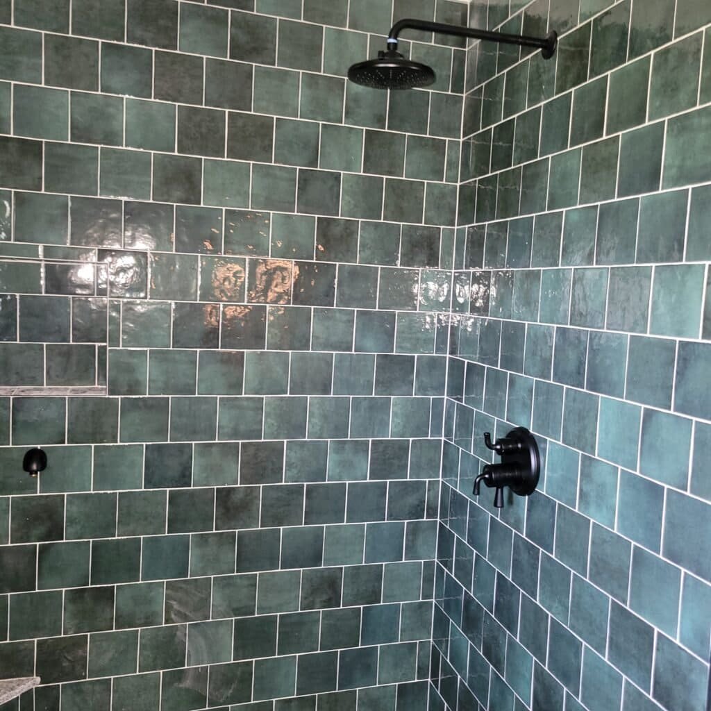 Green tiled shower wall with black showerhead and controls.