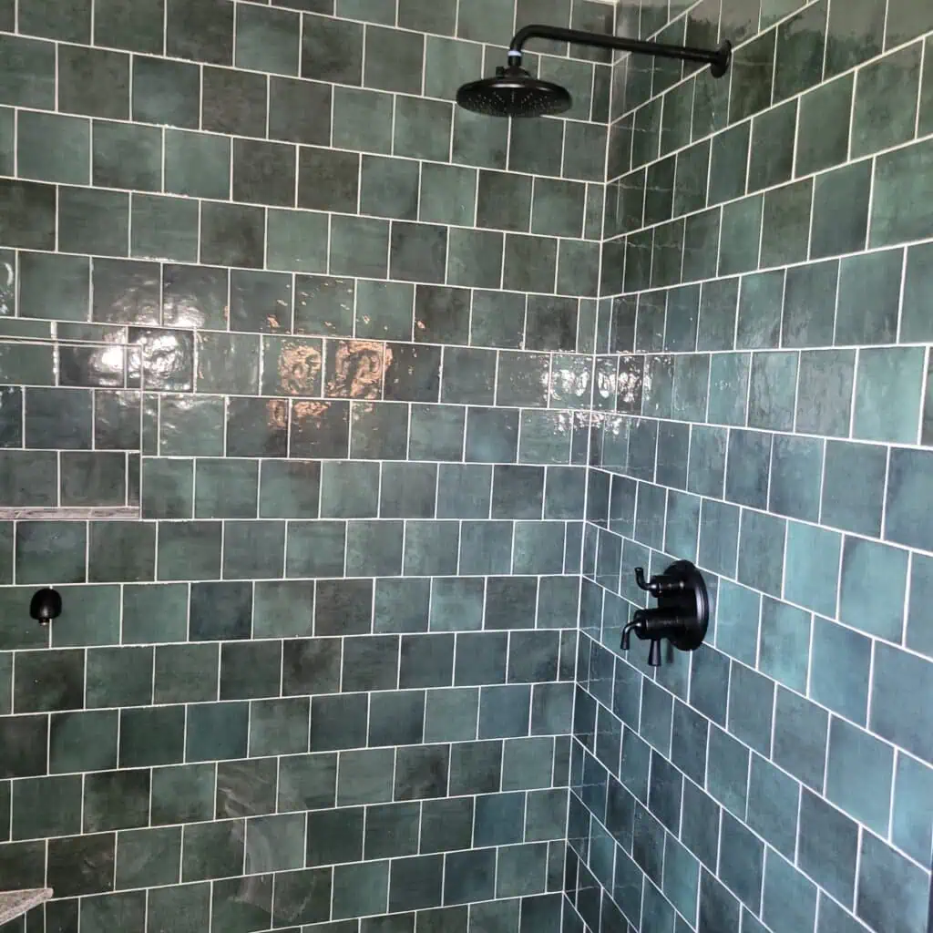 Green tiled shower wall with black showerhead and controls.