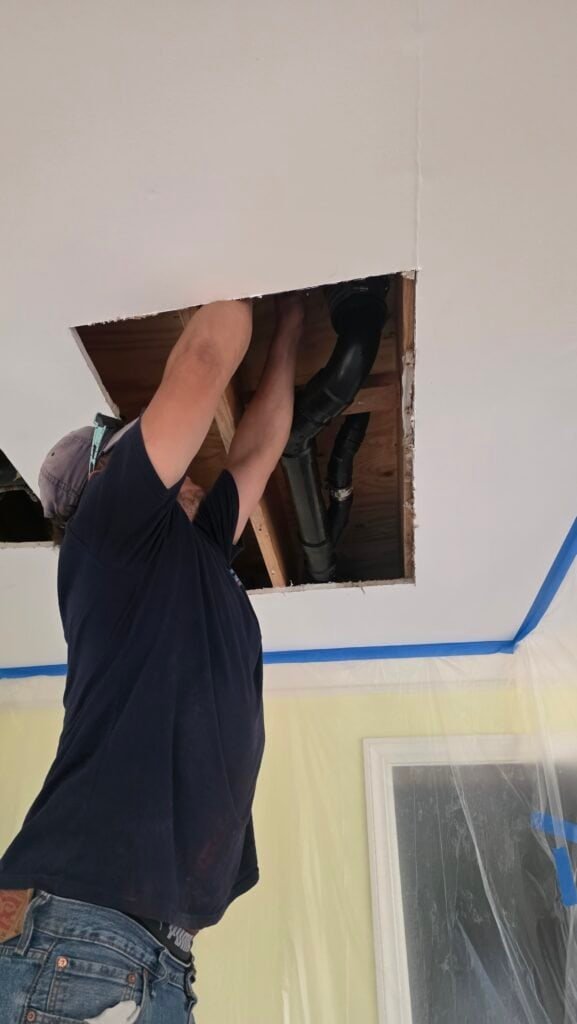 Professional plumber repairing ceiling pipes in a home.