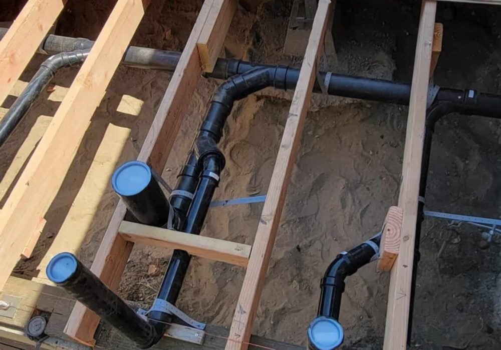 Plumbing pipes and tools installed on a wooden floor frame during construction.