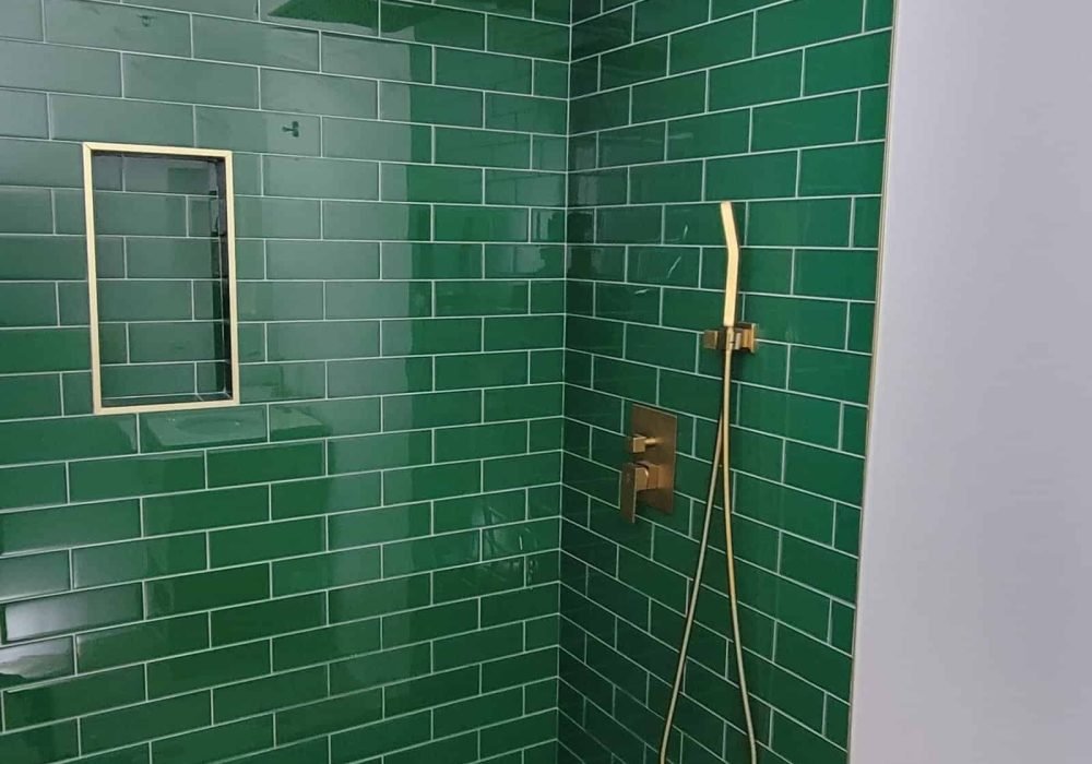 Green tiled shower with gold fixtures and rainfall showerhead.