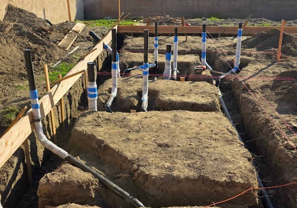 Excavation site for plumbing installation with exposed pipes and foundation work.